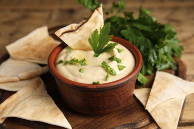 Photo of Delicious hummus with pita chips and parsley on wooden board, closeup