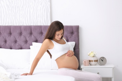 Happy pregnant woman sitting on bed at home