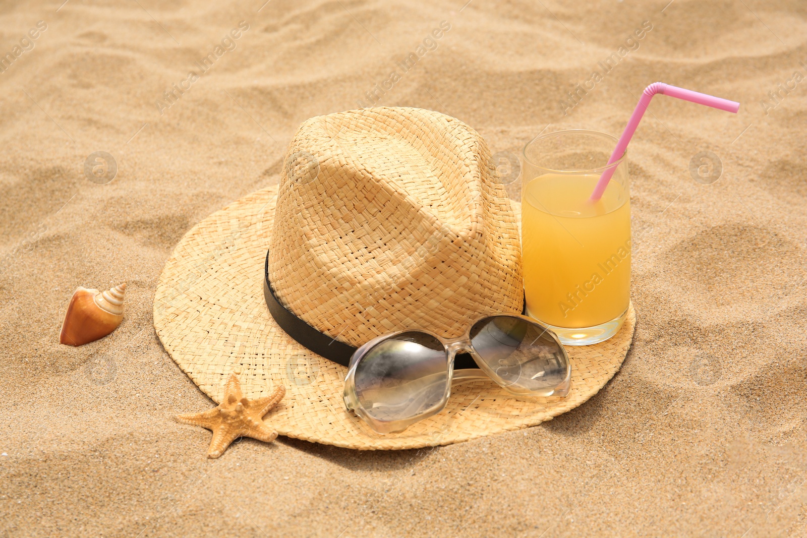 Photo of Straw hat, sunglasses and refreshing drink on sand. Beach accessories