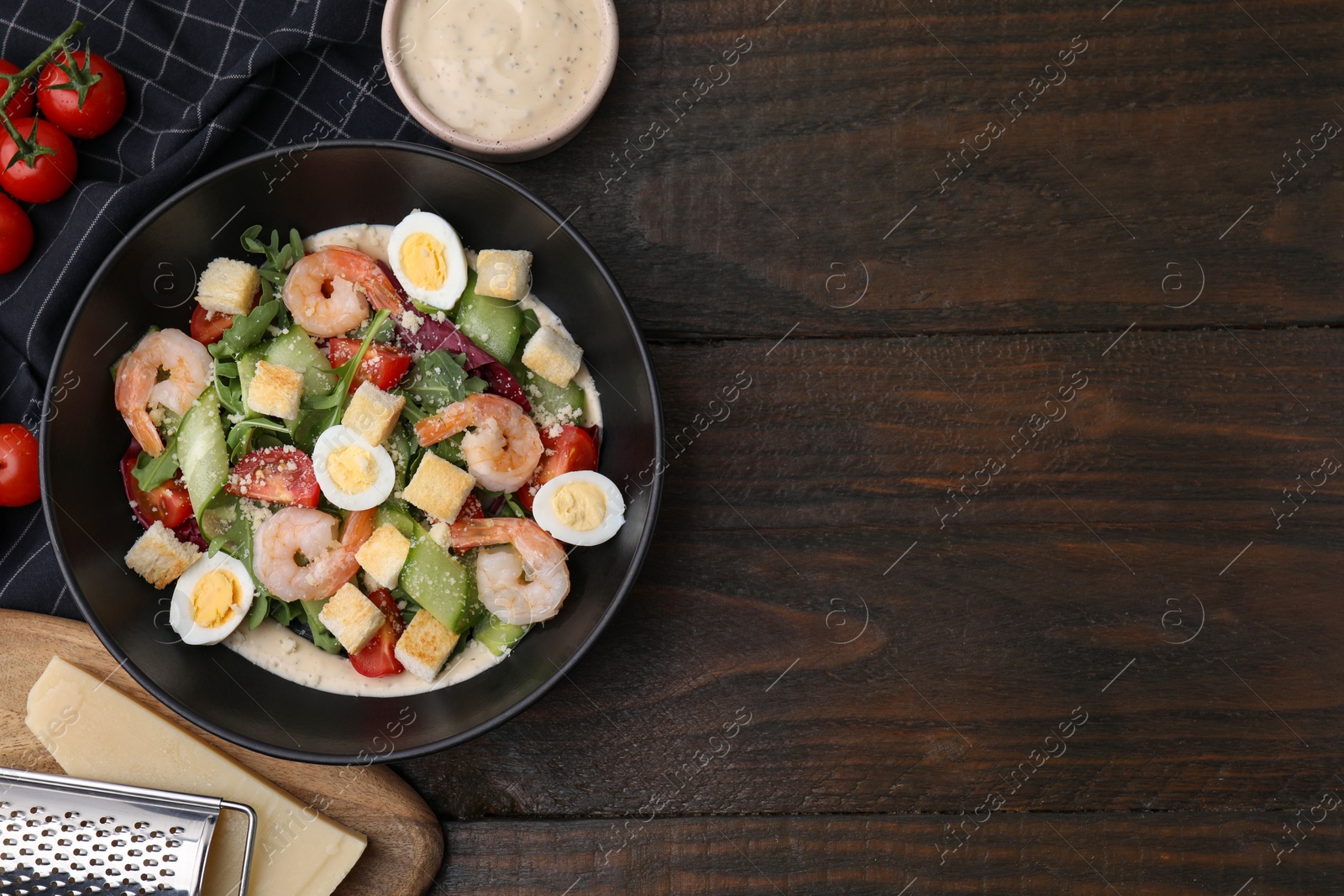 Photo of Delicious Caesar salad with shrimps and ingredients on wooden table, flat lay. Space for text