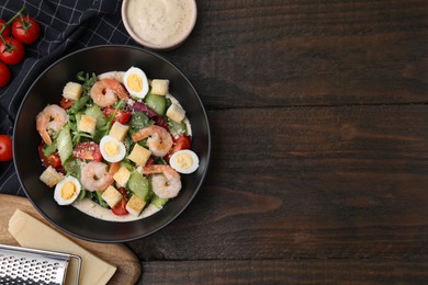 Photo of Delicious Caesar salad with shrimps and ingredients on wooden table, flat lay. Space for text