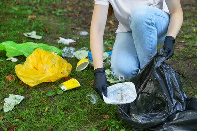Photo of Woman with plastic bag collecting garbage on green grass, closeup