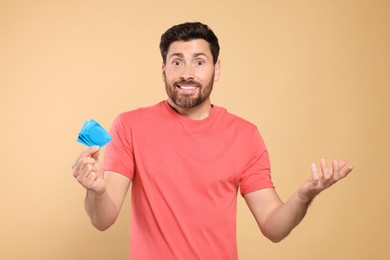 Photo of Confused man holding condoms on beige background. Safe sex