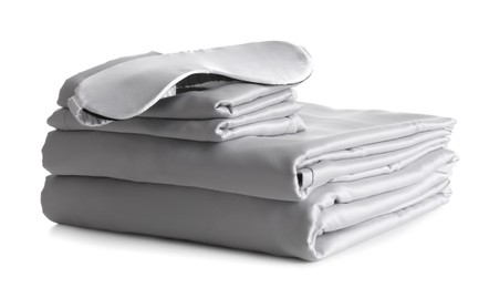 Photo of Stack of clean silky bed linen and sleeping mask isolated on white