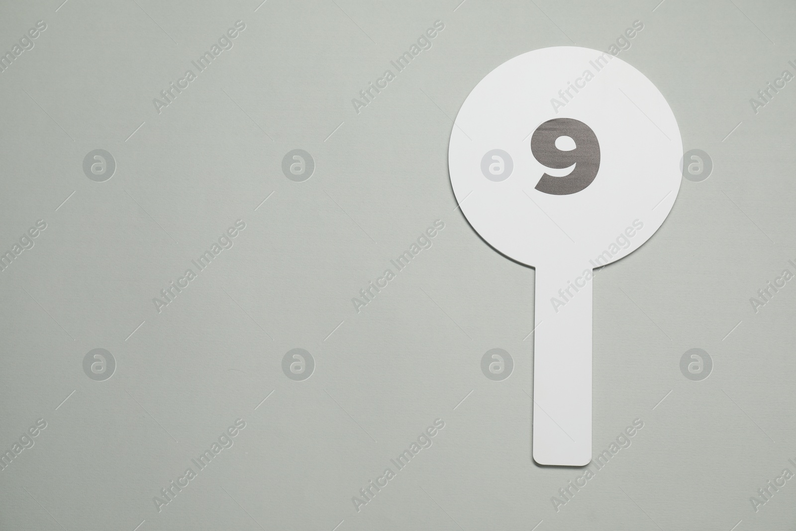 Photo of Auction paddle with number 9 on light grey background, top view. Space for text