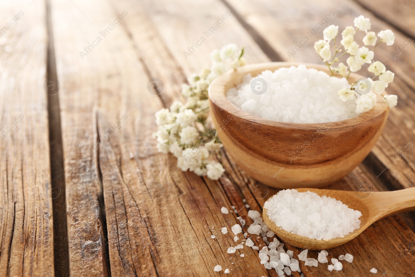 Photo of Aromatic sea salt and beautiful flowers on wooden table. Space for text