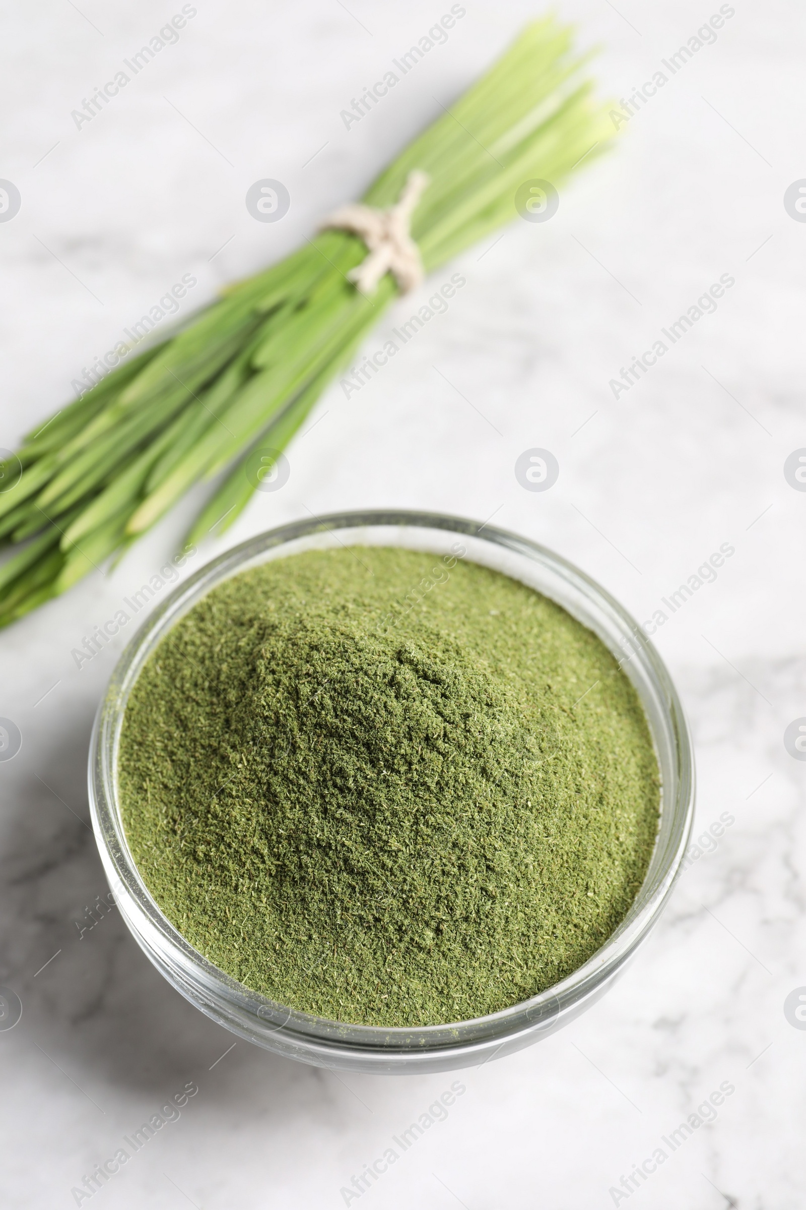 Photo of Wheat grass powder in glass bowl on white marble table, closeup