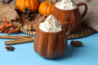 Mugs of pumpkin spice latte with whipped cream on light blue wooden table