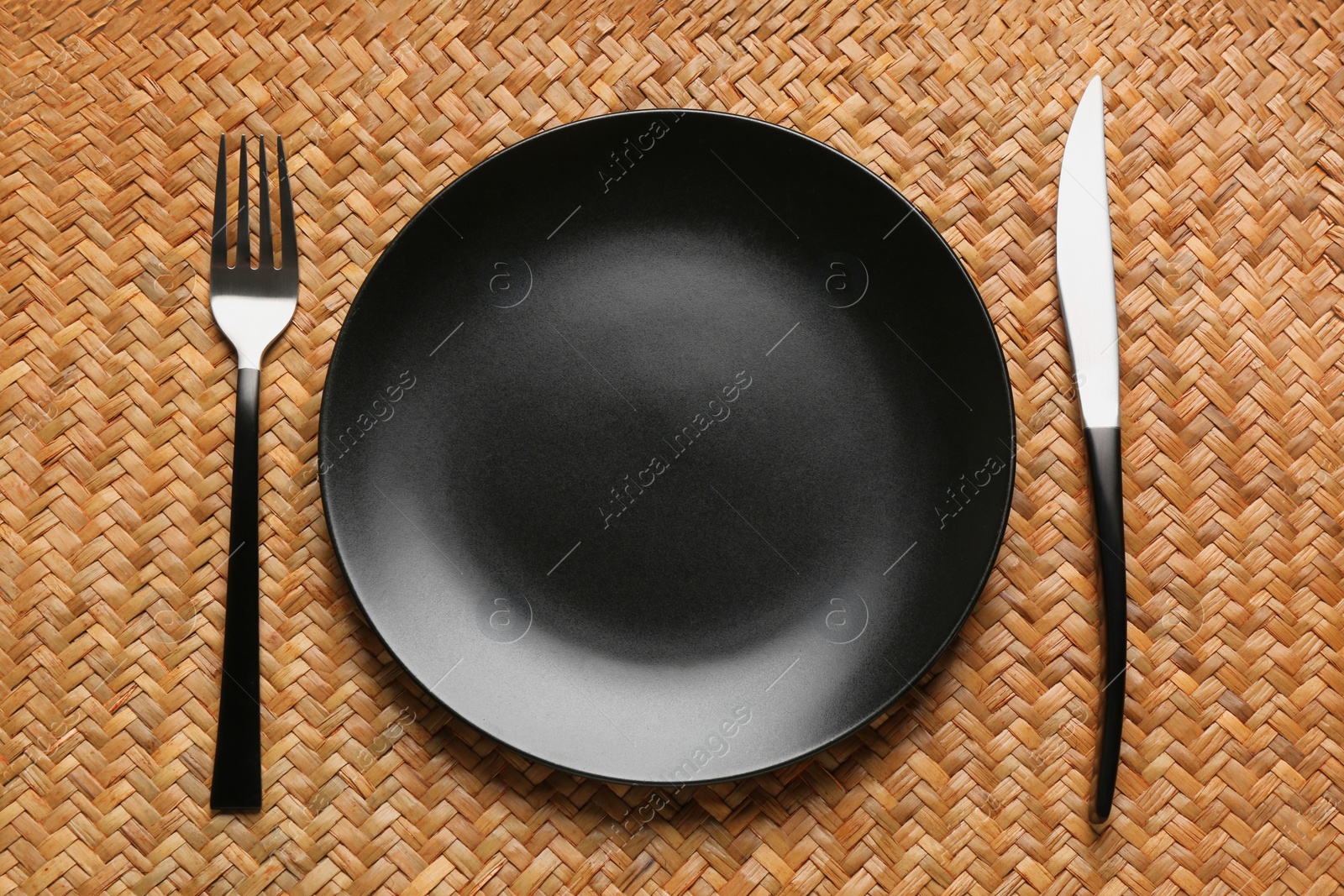 Photo of Clean plate and shiny silver cutlery on wicker mat, flat lay