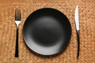 Photo of Clean plate and shiny silver cutlery on wicker mat, flat lay