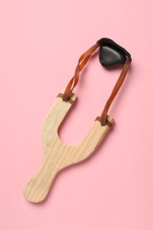 Photo of Wooden slingshot with pebble on pink background, top view