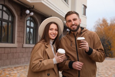 Photo of Happy couple wearing stylish autumn clothes with cups of coffee on city street