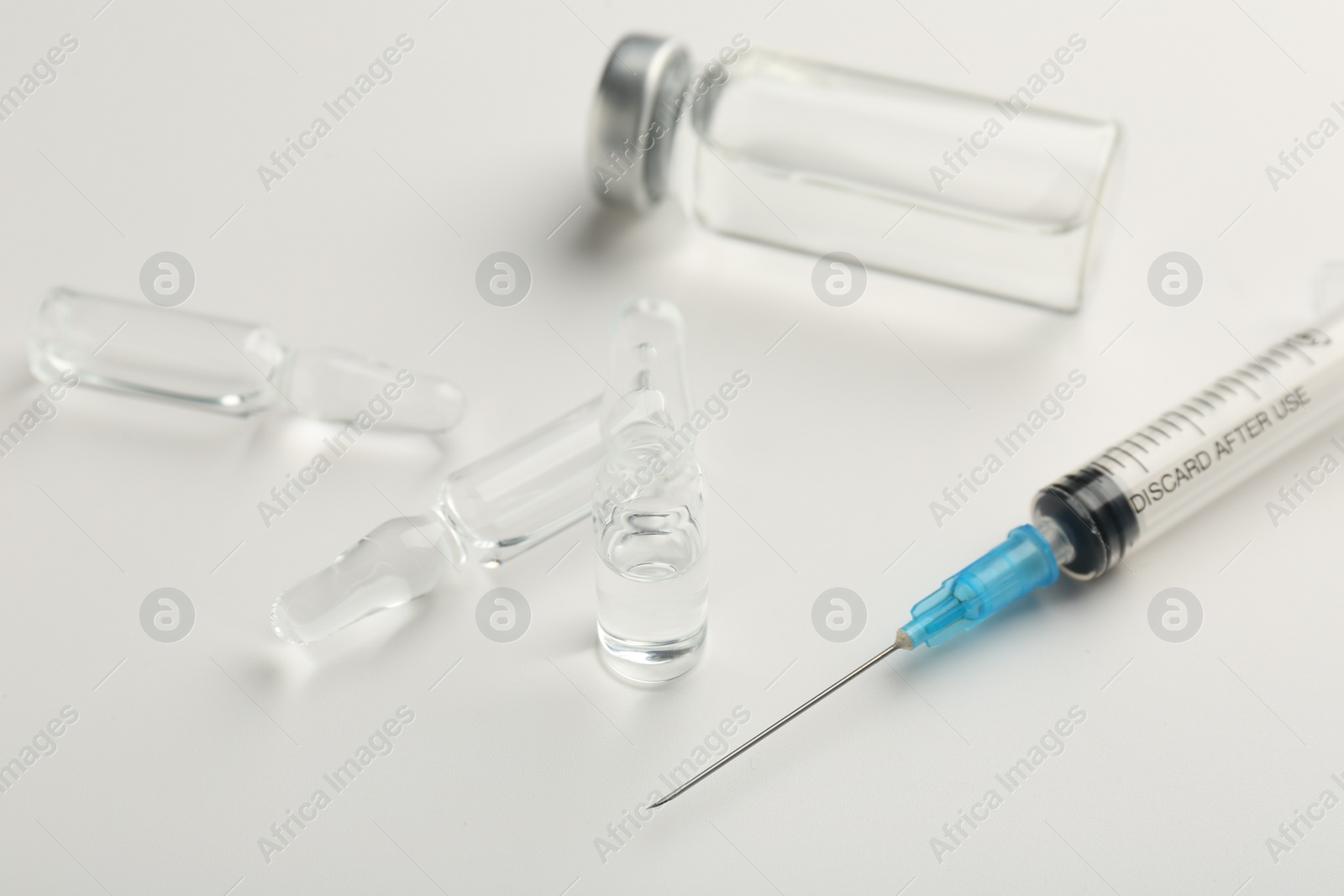 Photo of Glass ampoules with liquid and syringe on white background, closeup