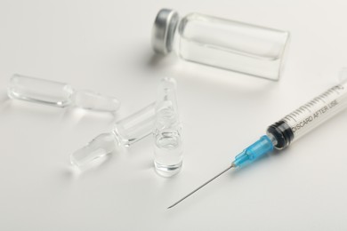 Photo of Glass ampoules with liquid and syringe on white background, closeup