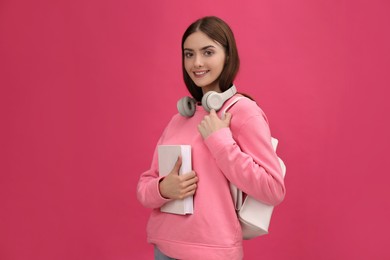 Photo of Teenage student with book, headphones and backpack on pink background
