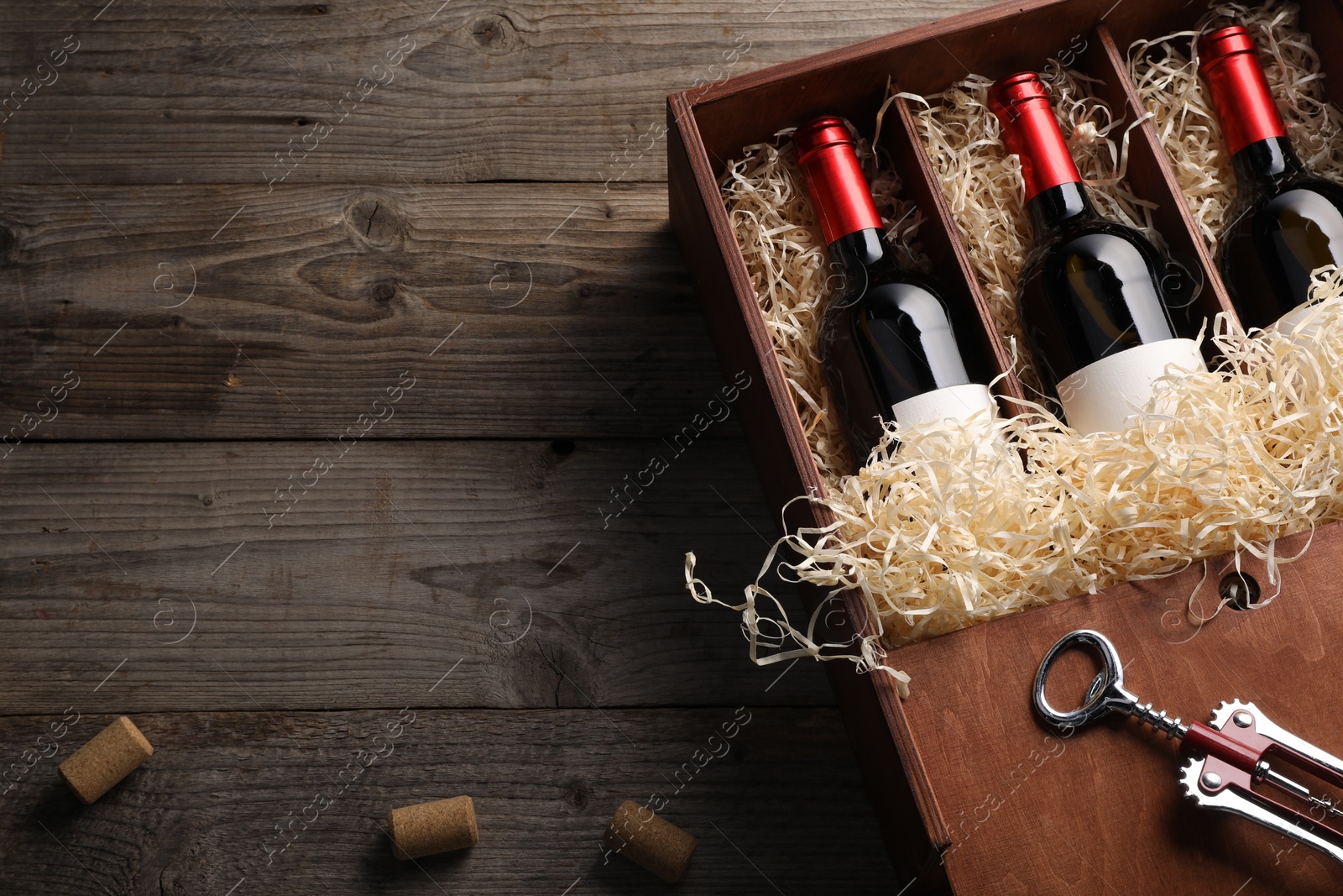 Photo of Box with wine bottles, corkscrew and corks on wooden table, flat lay. Space for text