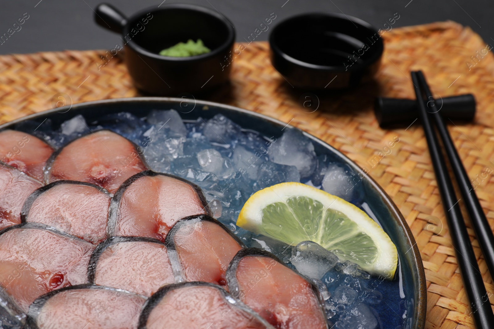 Photo of Raw mackerel slices, ice cubes, lemon served with vasabi and soy sauce on wicker mat, closeup. Fish delicacy