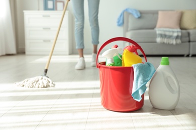 Photo of Woman washing floor with mop at home, focus on bucket and cleaning supplies