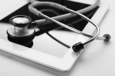 Photo of Medical stethoscope and tablet on beige background, closeup