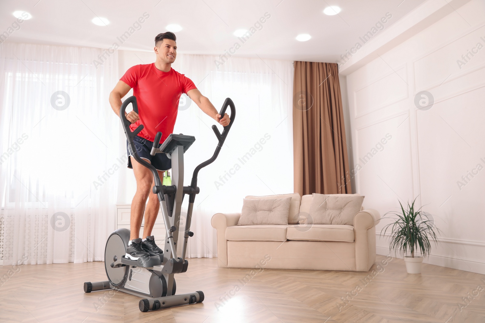 Photo of Man using modern elliptical machine at home