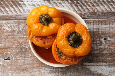 Photo of Tasty stuffed peppers in bowl on wooden rustic table, top view