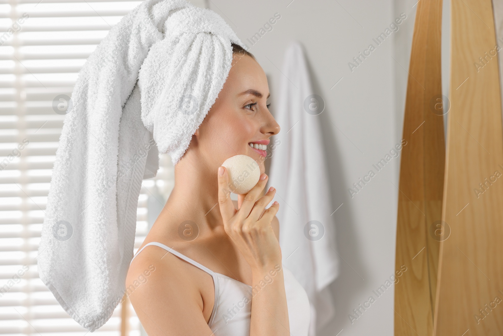 Photo of Happy young woman washing her face with sponge in bathroom