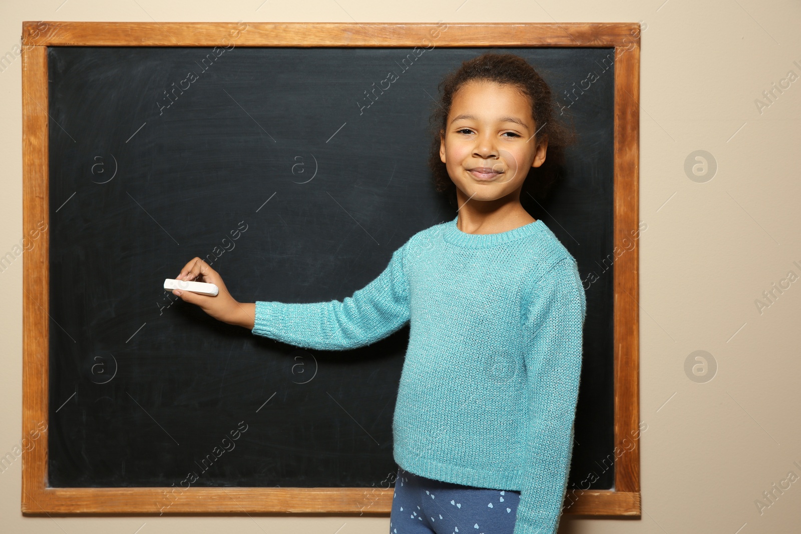 Photo of African-American child drawing with chalk on blackboard. Space for text