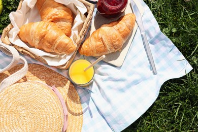 Blanket with juice, jam and croissants for picnic on green grass, flat lay