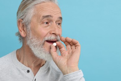 Photo of Senior man taking pill on light blue background. Space for text