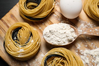 Photo of Raw linguine pasta and products on wooden board, flat lay