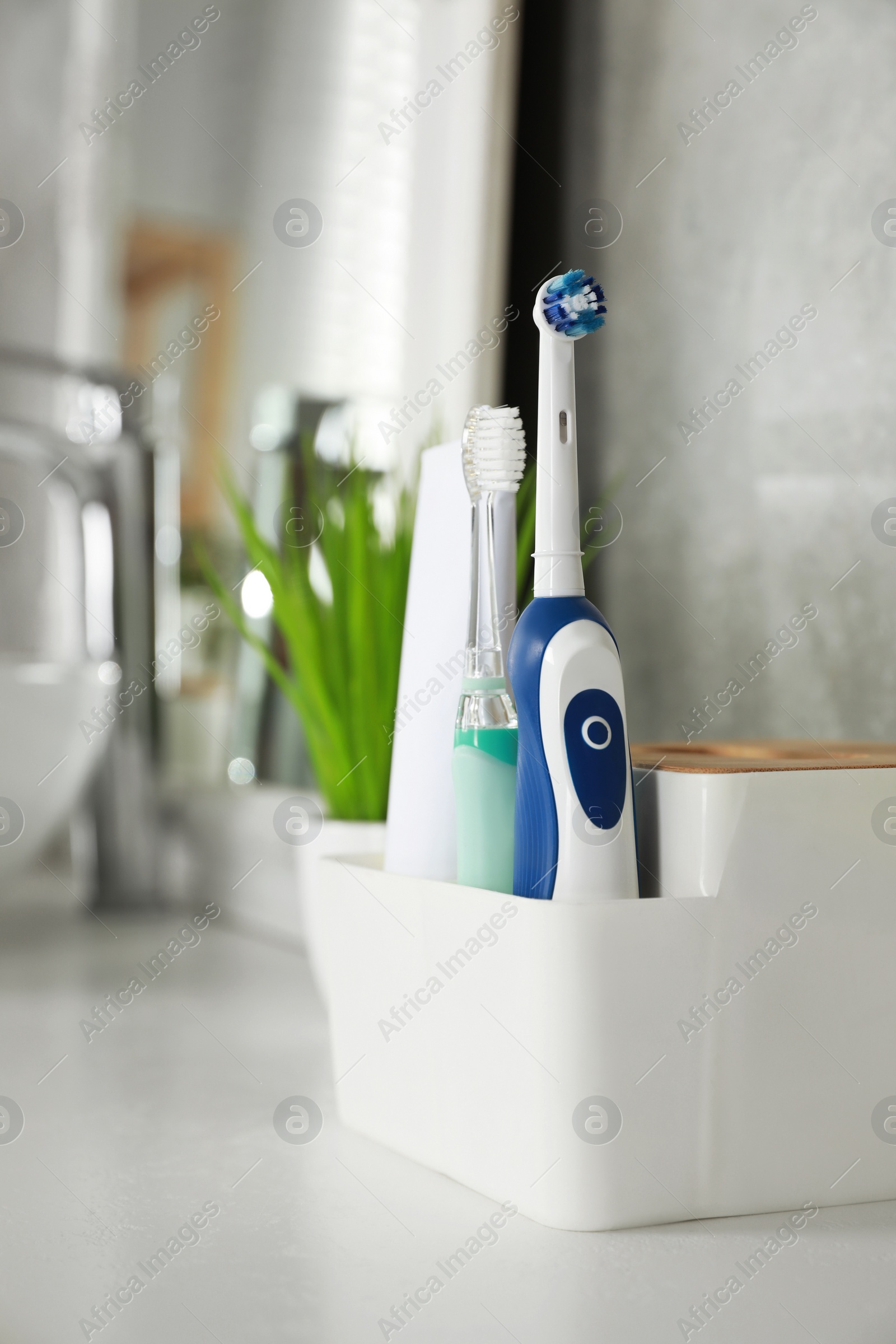 Photo of Electric toothbrushes and tube of paste on white countertop in bathroom