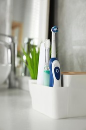 Electric toothbrushes and tube of paste on white countertop in bathroom