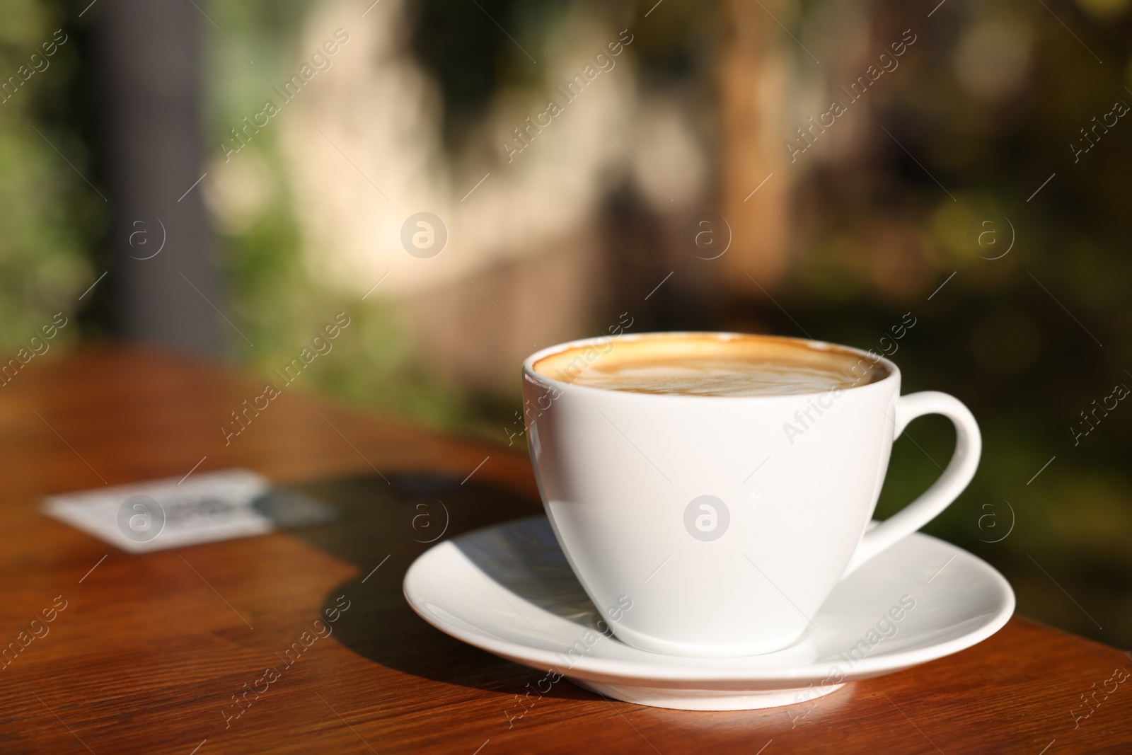 Photo of Cup of aromatic coffee with foam on table in outdoor cafe. Space for text