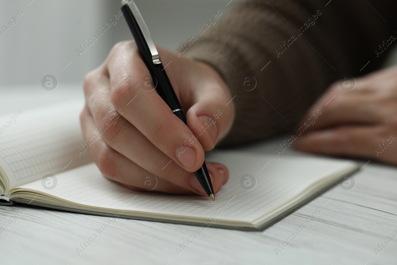 Photo of Man writing in notebook at white wooden table, closeup