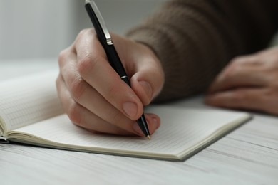 Man writing in notebook at white wooden table, closeup