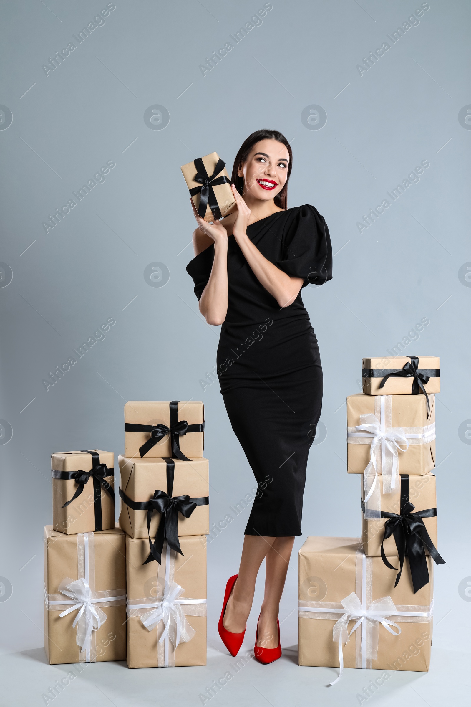 Photo of Woman in black dress with Christmas gifts on grey background