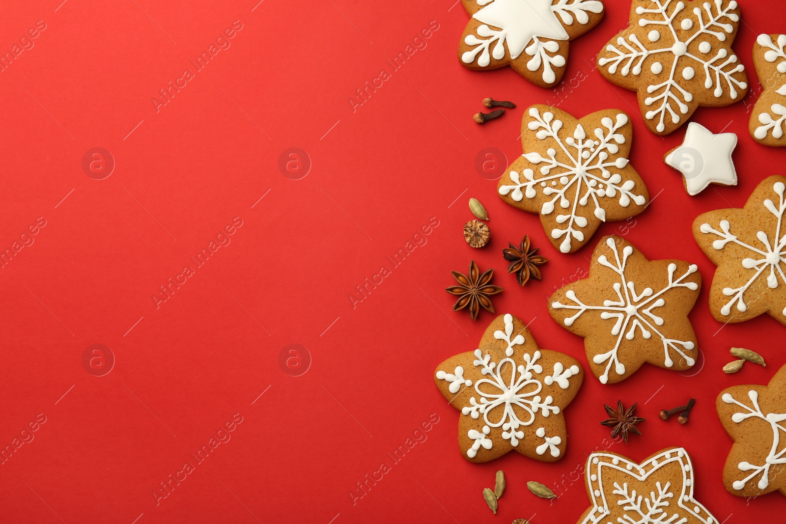 Photo of Tasty star shaped Christmas cookies with icing and spices on red background, flat lay. Space for text