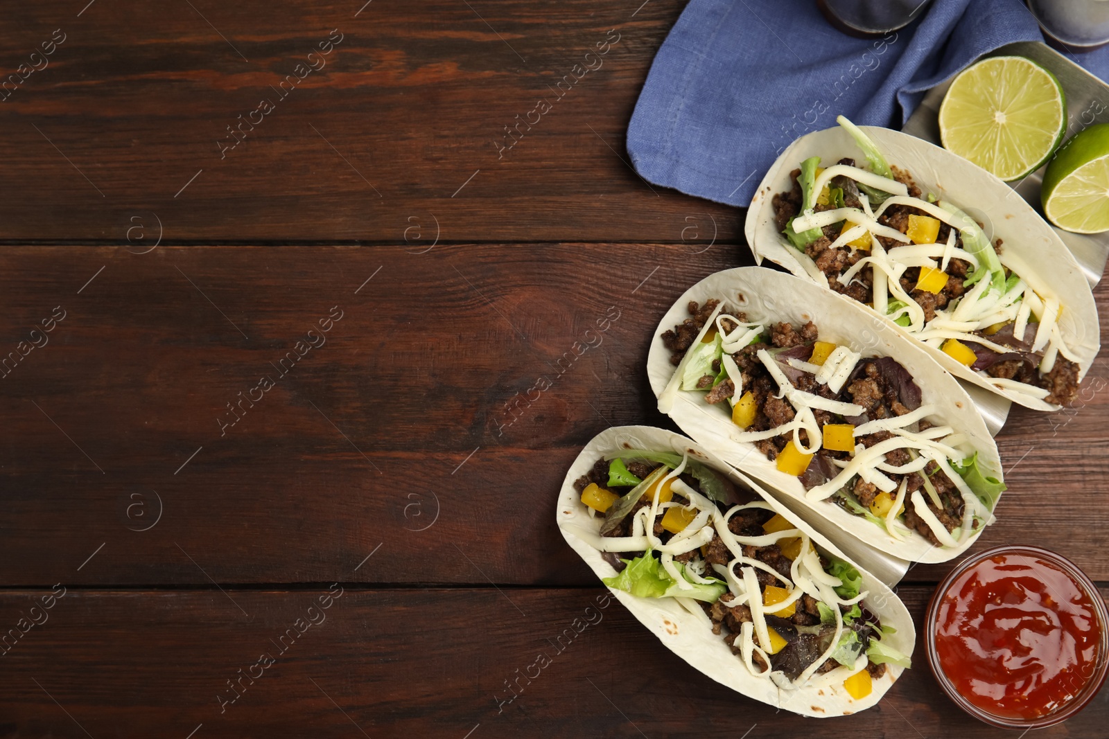 Photo of Delicious tacos with fried meat, cheese and lime on wooden table, flat lay. Space for text