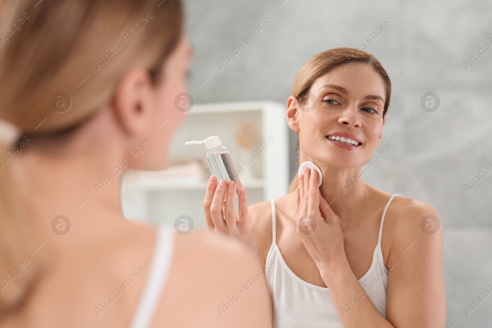 Photo of Beautiful woman removing makeup with cotton pad near mirror indoors