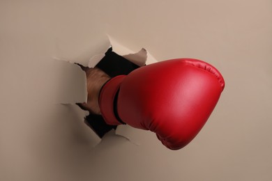 Photo of Man breaking through beige paper with boxing glove, closeup