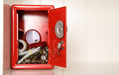 Photo of Open red steel safe with money and jewelry on shelf. Space for text