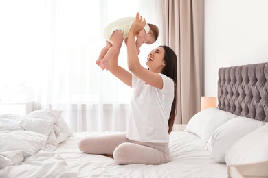 Photo of Young mother playing with her cute baby on bed indoors