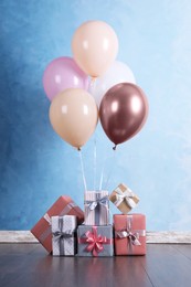 Bunch of color balloons and beautifully wrapped gift boxes near light blue wall indoors
