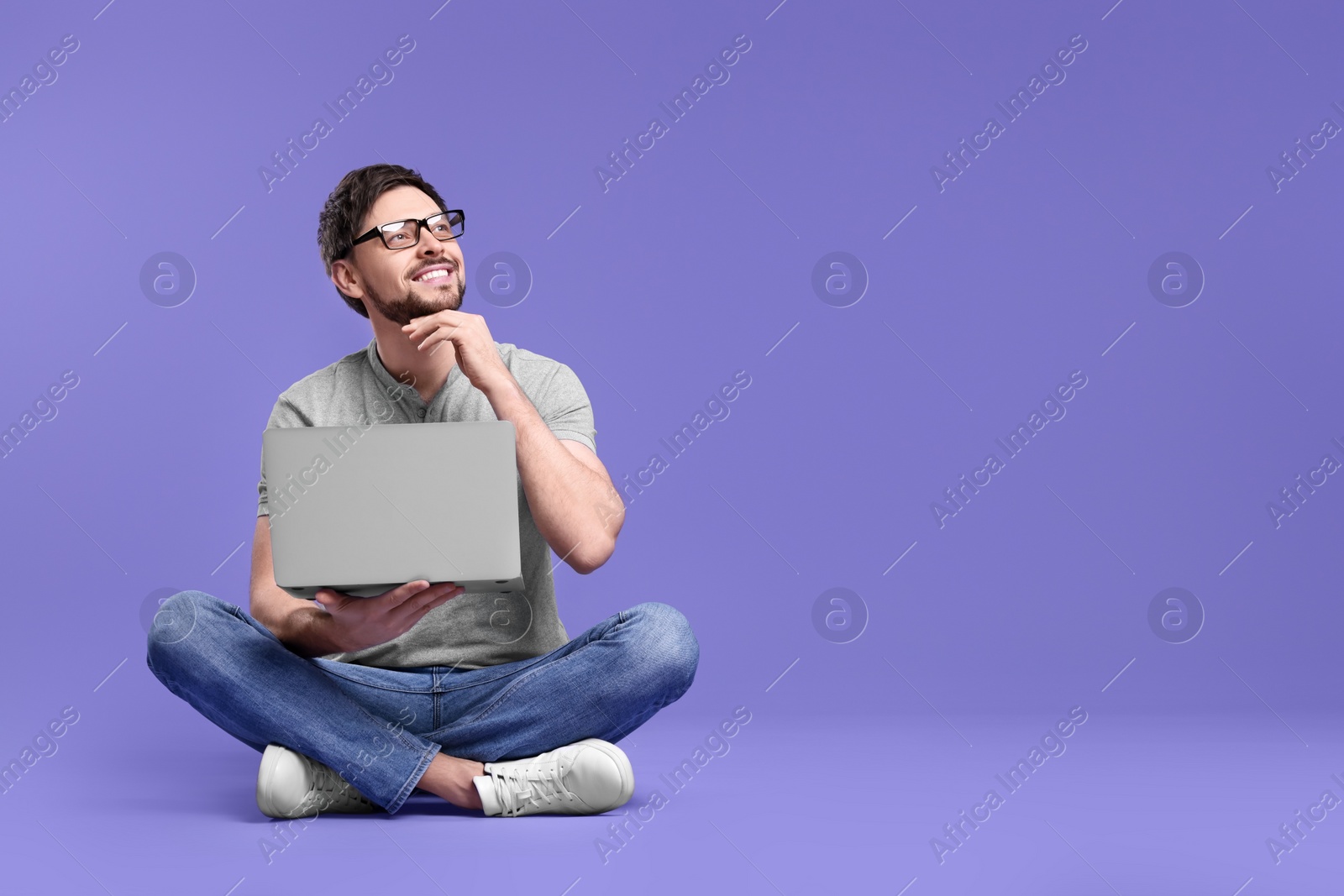Photo of Happy man with laptop on lilac background, space for text
