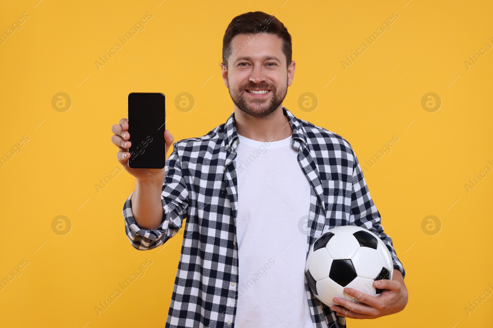 Photo of Happy sports fan with ball and smartphone on yellow background