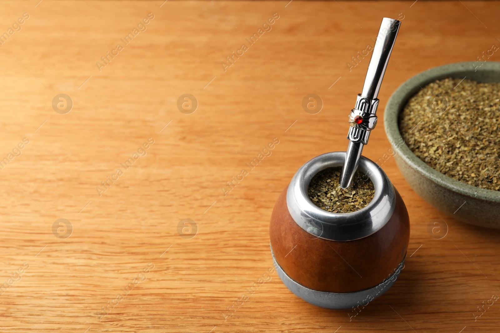 Photo of Calabash with mate tea and bombilla on wooden table. Space for text