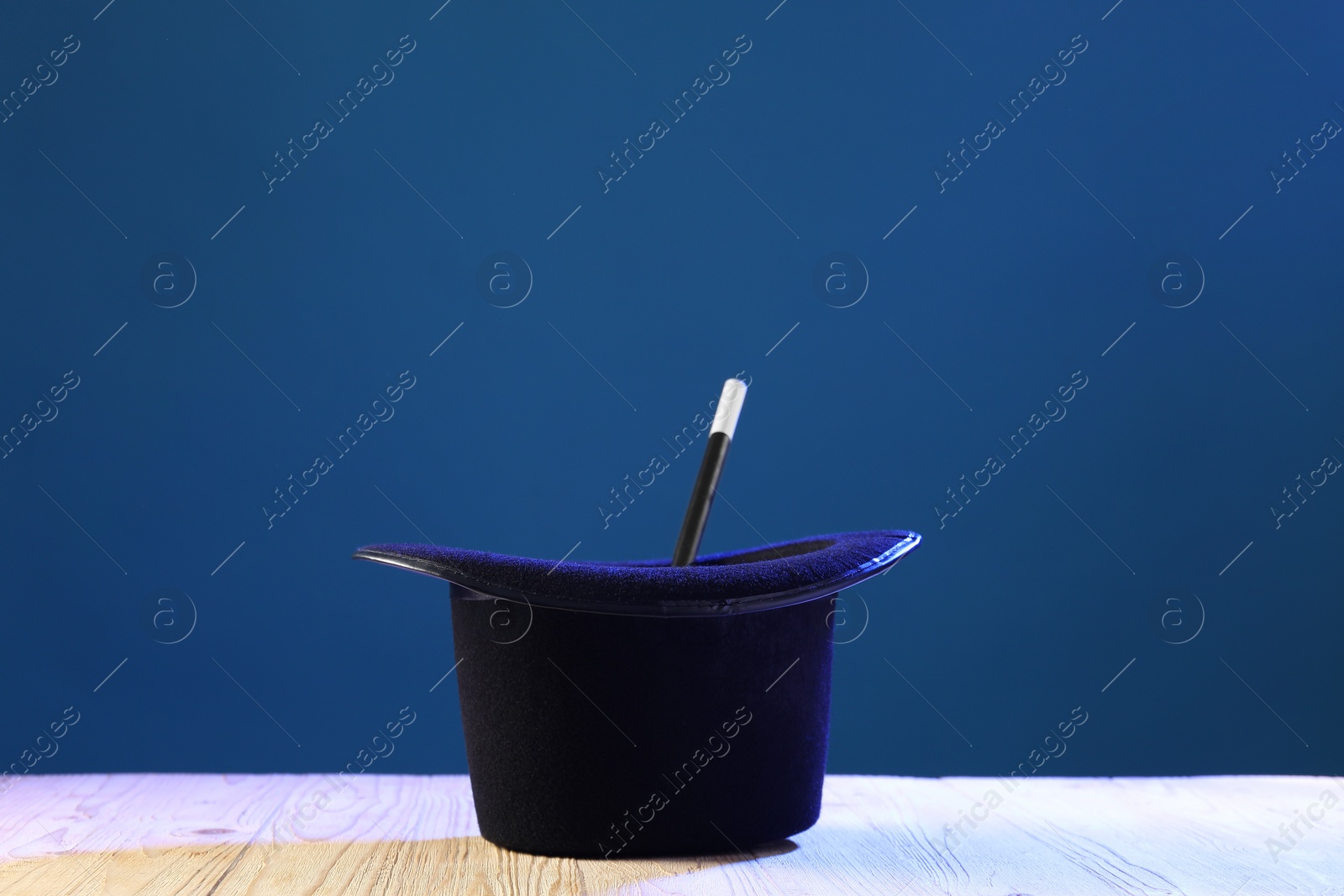 Photo of Magician's hat and wand on wooden table against blue background