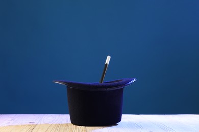 Magician's hat and wand on wooden table against blue background