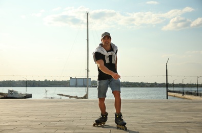 Photo of Handsome young man roller skating on pier near river