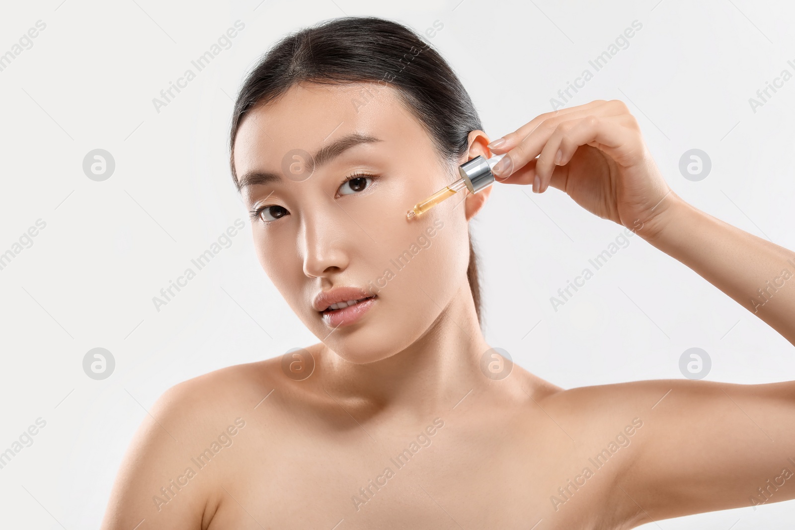 Photo of Beautiful young woman applying cosmetic serum onto her face on white background